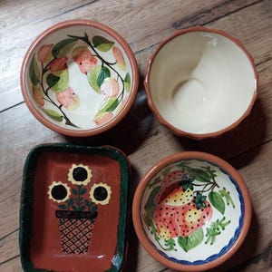 May include: Four ceramic bowls with hand-painted designs. One bowl features a floral design with sunflowers, another has a fruit design with strawberries, and two bowls have a fruit design with apples. The bowls are all brown with a green rim.