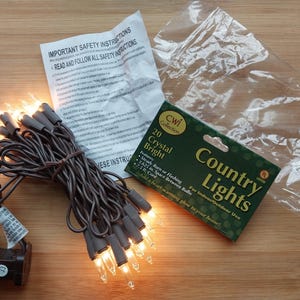 May include: A package of 20 crystal bright country lights with a brown wire. The package is labeled "20 Crystal Bright Country Lights" and includes instructions for indoor and outdoor use. The lights are strung together and ready to be used.