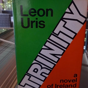 May include: A green, white, and orange paperback book with the title "TRINITY" in large, bold, white letters. The author's name, "Leon Uris", is printed in black letters above the title. The book cover also includes the text "a novel of Ireland".