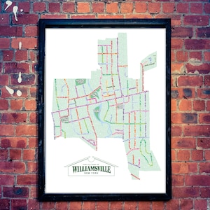 Könnte beinhalten: Gerahmter Karten-Druck von Williamsville, New York, mit detailliertem Straßenverlauf in verschiedenen Farben. Die Karte befindet sich vor einem weißen Hintergrund in einem schwarzen Rahmen, montiert an einer roten Backsteinmauer. Der Text "The Village of Williamsville New York" befindet sich unten.