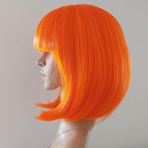 May include: Bright orange bob wig with blunt bangs. The wig is styled on a mannequin head, showcasing the vibrant color and sleek cut. The wig's synthetic fibers create a smooth, shiny appearance, perfect for cosplay or costume parties.