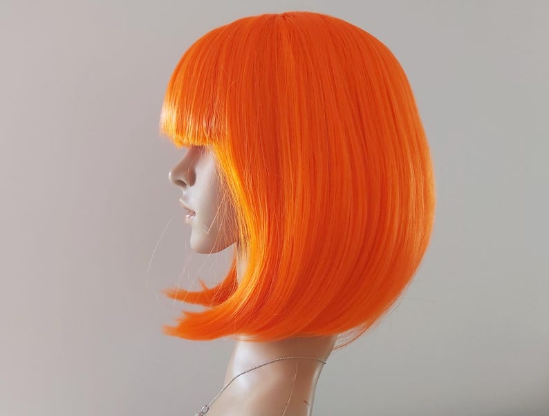 May include: Bright orange bob wig with blunt bangs. The wig is styled on a mannequin head, showcasing the vibrant color and sleek cut. The wig's synthetic fibers create a smooth, shiny appearance, perfect for cosplay or costume parties.