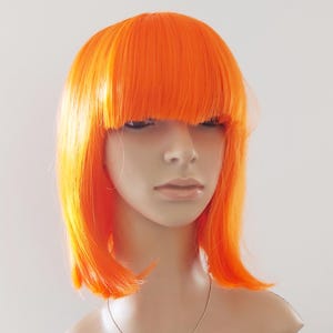 May include: Bright orange wig with a blunt fringe and shoulder-length cut. The wig is styled on a mannequin head, showcasing its vibrant color and sleek design. The wig is a bold fashion statement.