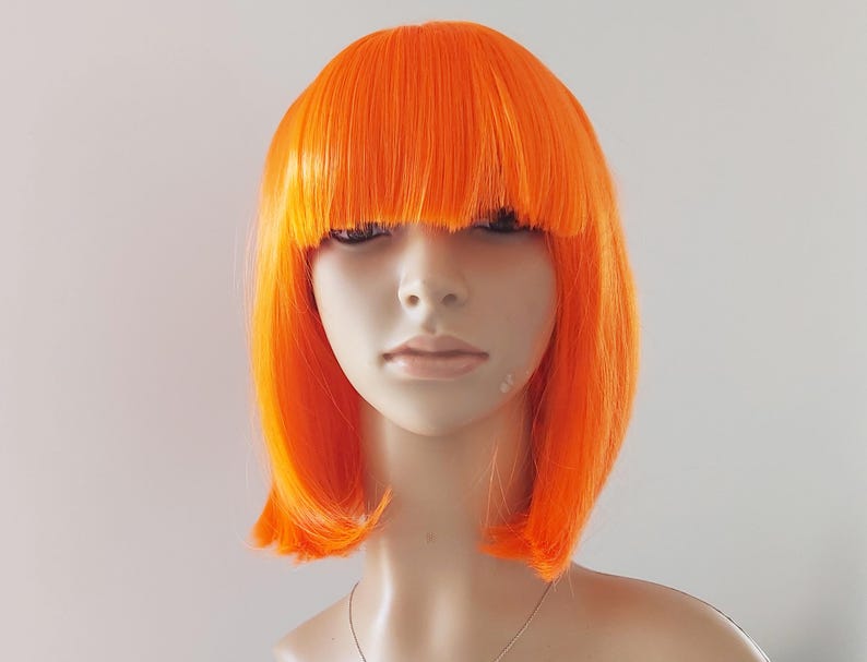 May include: A vibrant orange wig with a blunt fringe and a bob cut. The wig is styled on a mannequin head, showcasing its bright color and sleek design. The wig's bold color makes it suitable for costume parties or theatrical performances.
