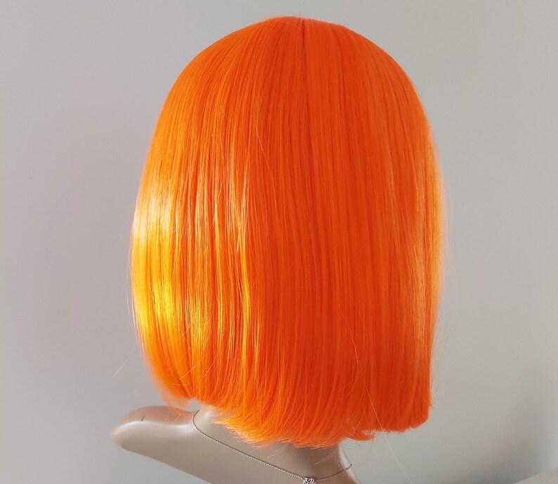 May include: Bright orange wig with a blunt cut, styled in a bob. The wig is displayed on a mannequin head against a plain background. The synthetic hair has a smooth, straight texture and a vibrant, solid color.
