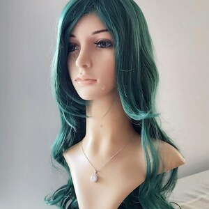May include: A long, wavy, teal green wig with a side part. The wig is styled with loose curls and is worn on a mannequin head.