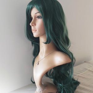 May include: A long, wavy, dark green wig with a side part. The wig is styled in loose curls and is worn on a mannequin head.