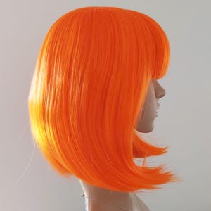 May include: Bright orange bob wig with blunt bangs. The wig is styled on a mannequin head, showcasing the vibrant color and sleek, straight hair. The wig's color is a bold, eye-catching shade of orange.