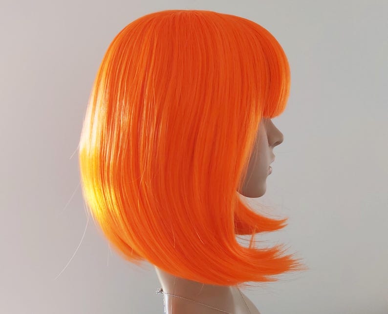 May include: Bright orange bob wig with blunt bangs. The wig is styled on a mannequin head, showcasing the vibrant color and sleek, straight hair. The wig's color is a bold, eye-catching shade of orange.