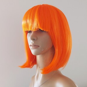 May include: Bright orange wig with a blunt fringe and a bob cut. The wig is styled on a mannequin head, showcasing its vibrant color and shape. The wig's synthetic fibers appear smooth and evenly colored.