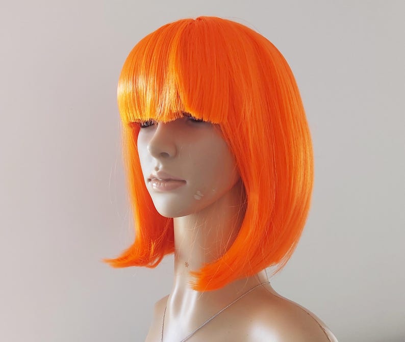 May include: Bright orange wig with a blunt fringe and a bob cut. The wig is styled on a mannequin head, showcasing its vibrant color and shape. The wig's synthetic fibers appear smooth and evenly colored.