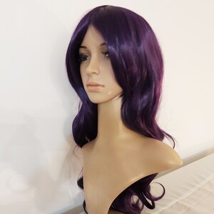 May include: A long, wavy purple wig with side-swept bangs. The wig is made of synthetic hair and is styled in a casual, everyday look.