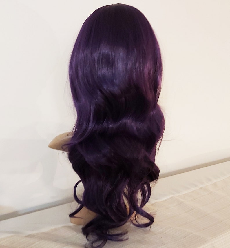 May include: A long, wavy, purple wig with a side part. The wig is styled in loose waves and is made of synthetic hair.