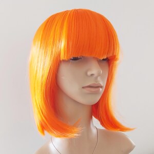 May include: A bright orange wig with a blunt fringe and shoulder-length layers. The wig is styled on a mannequin head, showcasing its vibrant color and sleek design. The wig's color is a bold, eye-catching shade of orange.