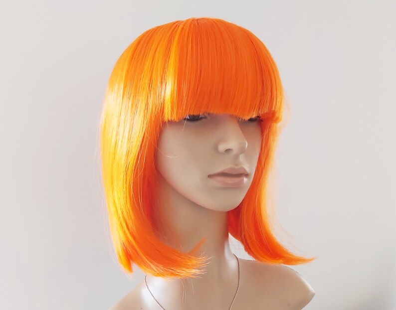 May include: A bright orange wig with a blunt fringe and shoulder-length layers. The wig is styled on a mannequin head, showcasing its vibrant color and sleek design. The wig's color is a bold, eye-catching shade of orange.