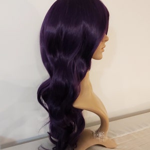 May include: A long, wavy, purple wig on a mannequin head. The wig has a side part and is styled in loose waves.