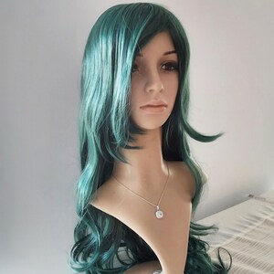 May include: A long, wavy, teal green wig with a side part. The wig is styled with loose waves and falls to the shoulders.