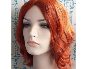 May include: A mannequin head with a vibrant, wavy, auburn wig. The wig features a side part and shoulder-length style. The mannequin has realistic features, including blue eyes and full lips. The background is a light blue and white patterned design.