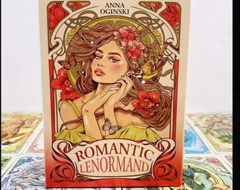 May include: A box of Romantic Lenormand playing cards with an art nouveau design featuring a woman with long brown hair, flowers, and a bird. The box is cream colored with red and gold accents. The text on the box reads "Anna Oginski" and "Romantic Lenormand".