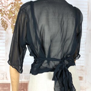 May include: Black sheer wrap top with short sleeves and a tie closure at the waist. The top is displayed on a mannequin, showcasing its delicate, flowing fabric. The garment's design is simple yet elegant, suitable for layering or as a standalone piece.