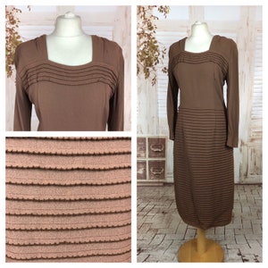 May include: A brown midi dress with long sleeves and a square neckline. The dress is made from a textured fabric with horizontal pleats throughout.