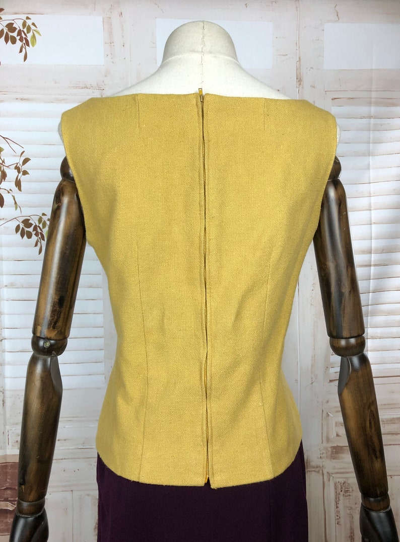 Pode incluir: Um top sem mangas amarelo mostarda com um z&iacute;per nas costas. O top &eacute; feito de um tecido texturizado e tem um design simples e cl&aacute;ssico.