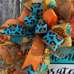 May include: A fall-themed wreath with a turquoise, orange, and brown ribbon bow. The wreath features a sign that says "Thankful, Grateful, Blessed".