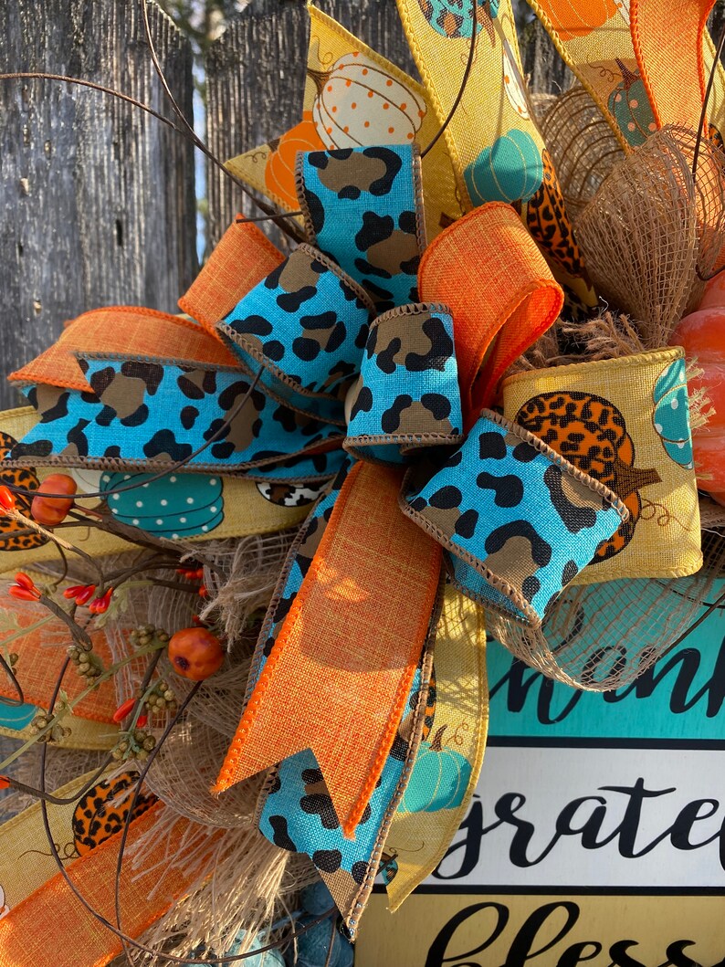 May include: A fall-themed wreath with a turquoise, orange, and brown ribbon bow. The wreath features a sign that says "Thankful, Grateful, Blessed".
