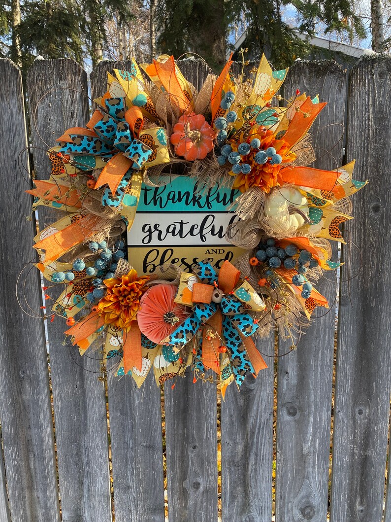 May include: A fall-themed wreath with orange, yellow, and blue accents. It features a sign that reads "thankful grateful and blessed".