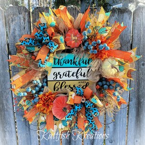 May include: A fall-themed wreath with orange, blue and brown accents. It features a sign that reads "thankful grateful and blessed".