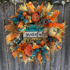 May include: A fall-themed wreath with orange, yellow, and blue accents. It features a sign that reads "thankful grateful and blessed".