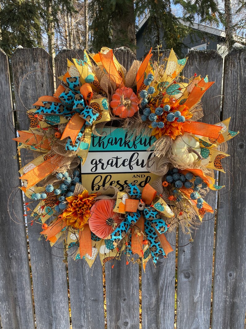 May include: A fall-themed wreath with orange, yellow, and blue accents. It features a sign that reads "thankful grateful and blessed".