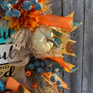 May include: A fall-themed wreath with orange, yellow, and blue accents. The wreath features a sign that reads "You are loved" and is decorated with burlap, faux pumpkins, and berries.