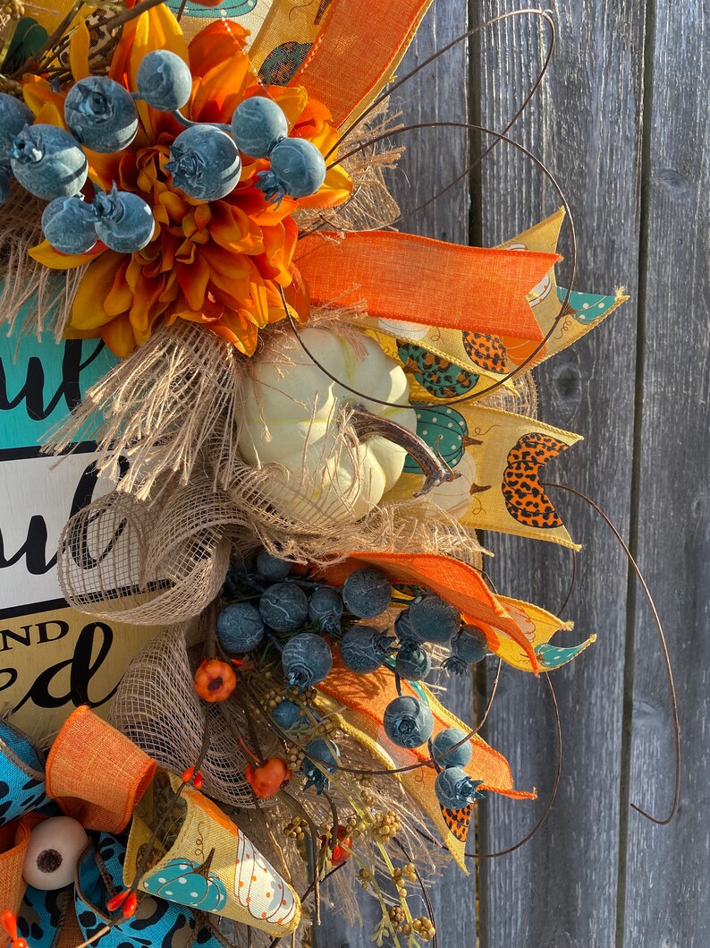 May include: A fall-themed wreath with orange, yellow, and blue accents. The wreath features a sign that reads "You are loved" and is decorated with burlap, faux pumpkins, and berries.
