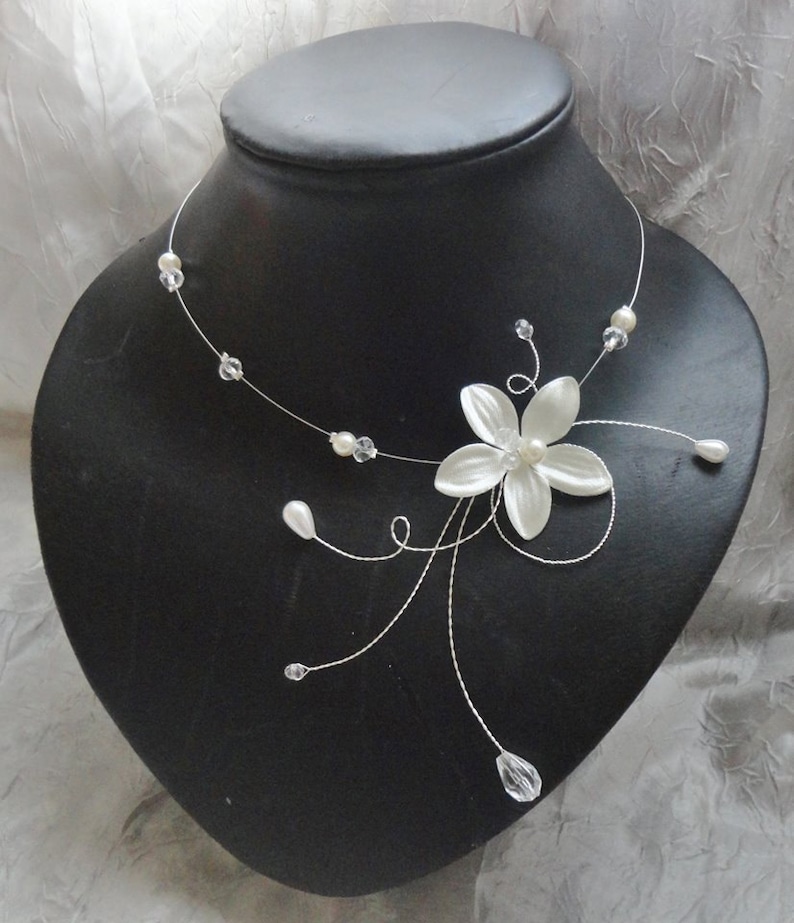 Peut inclure: Un collier d&eacute;licat de fleurs blanches avec des accents de cristal et de perles. Le collier est fait de fil fin et pr&eacute;sente une seule fleur blanche avec un centre de perle.