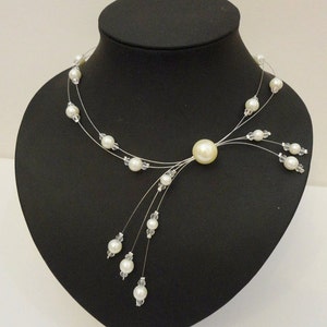 Peut inclure: Un collier d&eacute;licat de perles blanches avec une seule perle plus grosse au centre et des brins de perles plus petites qui pendent.