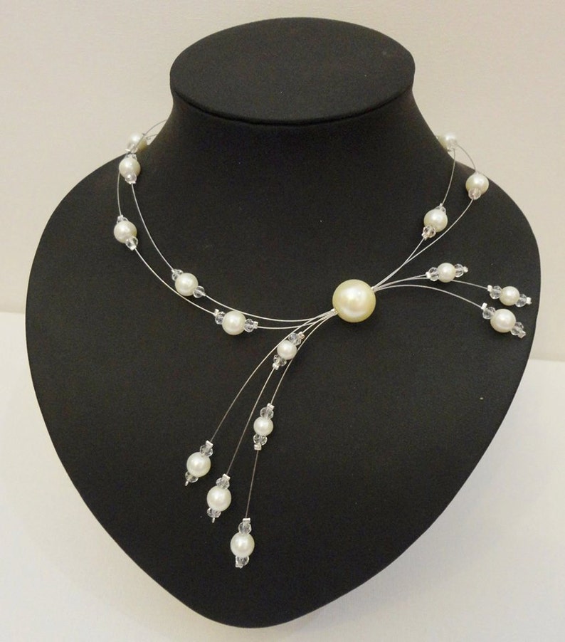 Peut inclure: Un collier d&eacute;licat de perles blanches avec une seule perle plus grosse au centre et des brins de perles plus petites qui pendent.