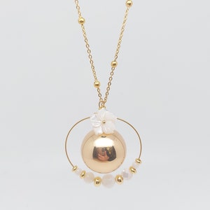 Pu&ograve; includere: Una collana d'oro con un ciondolo rotondo e un ciondolo a forma di fiore bianco. Il ciondolo &egrave; circondato da un cerchio di perline dorate e perle bianche.