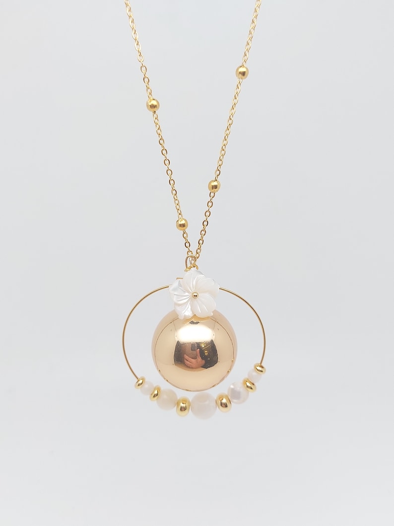 Pu&ograve; includere: Una collana d'oro con un ciondolo rotondo e un ciondolo a forma di fiore bianco. Il ciondolo &egrave; circondato da un cerchio di perline dorate e perle bianche.
