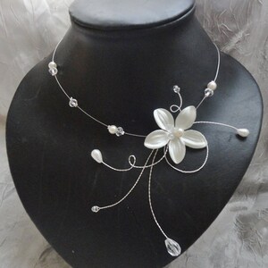 Peut inclure: Un collier d&eacute;licat en forme de fleur blanche avec des accents de perles et de cristaux. Le collier est fait de fil d'argent et pr&eacute;sente une seule fleur blanche avec un centre de perle.