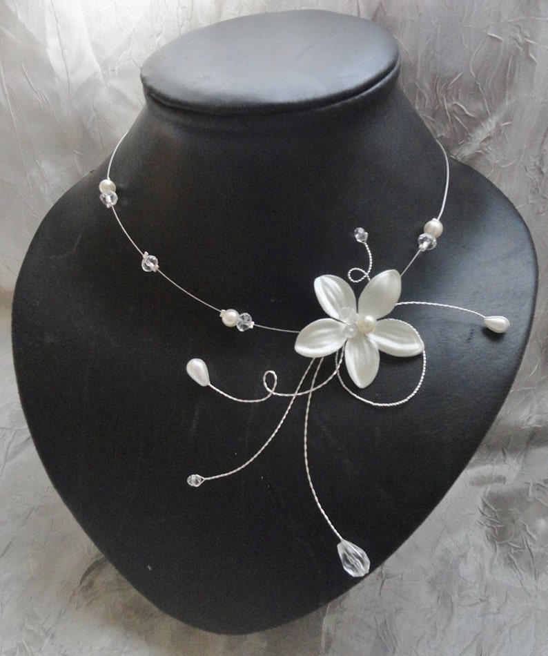 Peut inclure: Un collier d&eacute;licat en forme de fleur blanche avec des accents de perles et de cristaux. Le collier est fait de fil d'argent et pr&eacute;sente une seule fleur blanche avec un centre de perle.