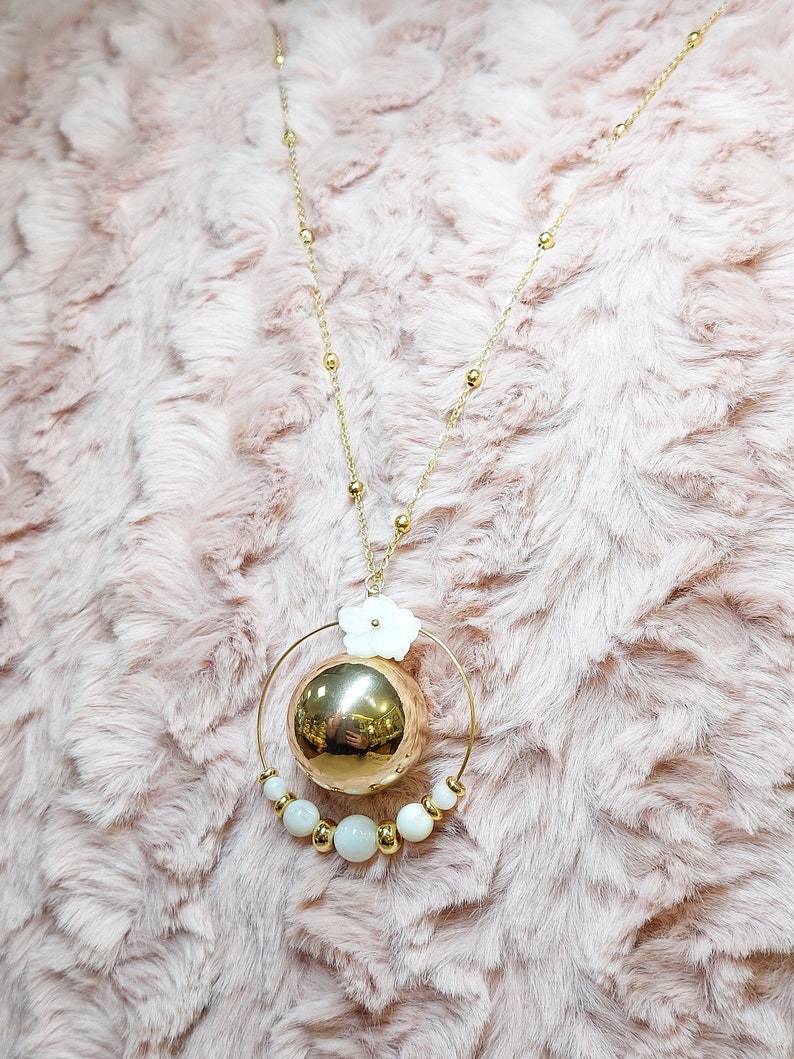 Pu&ograve; includere: Una collana d'oro con un grande ciondolo a forma di sfera dorata circondato da un cerchio di perle bianche e un ciondolo a forma di fiore bianco.