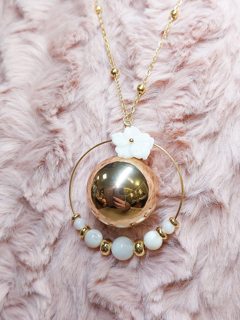 Pu&ograve; includere: Una collana d'oro con un grande ciondolo rotondo in oro e un ciondolo a forma di fiore bianco. Il ciondolo &egrave; circondato da un cerchio di perle bianche.