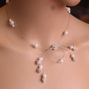 May include: A delicate silver necklace with a cluster of small white pearls and sparkling rhinestones. The necklace features a unique design with multiple strands that extend from a central point.