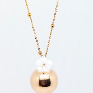 May include: Gold-toned necklace featuring a large, round pendant with a white flower accent. The chain has small gold beads and a delicate link design. The pendant reflects light, creating a polished look. A stylish piece of jewelry.