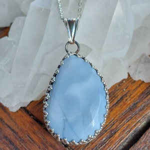Peut inclure: Un collier en argent avec un pendentif en opale bleu clair. Le pendentif est serti dans une bélière en argent avec une bordure décorative.