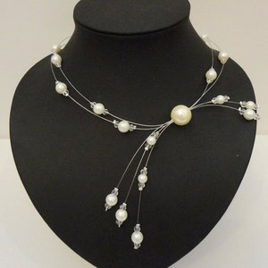 Peut inclure: Un collier d&eacute;licat en perles blanches avec un pendentif en perle plus grand et un design en cascade de petites perles.