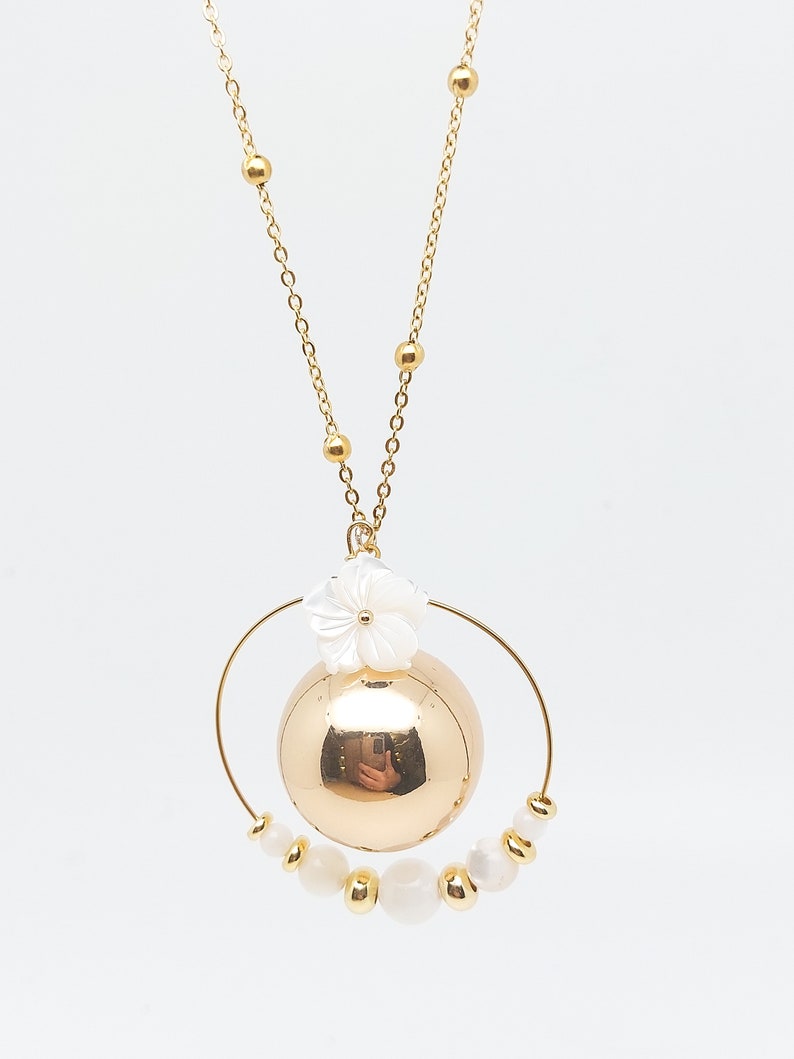 Pu&ograve; includere: Una collana d'oro con un grande ciondolo a forma di sfera dorata circondato da un cerchio di perle bianche e un ciondolo a forma di fiore bianco.