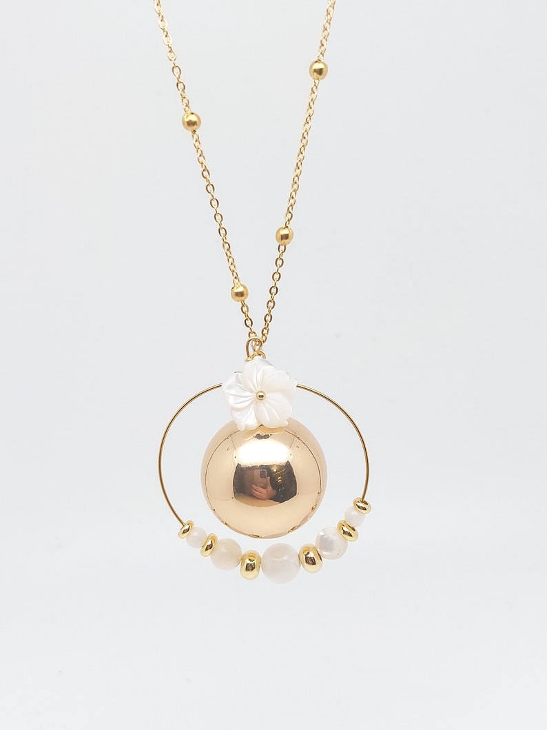 Pu&ograve; includere: Una collana d'oro con un ciondolo rotondo d'oro e un ciondolo a forma di fiore bianco. Il ciondolo &egrave; circondato da un cerchio di perle bianche.