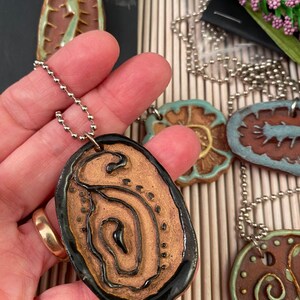 May include: A set of four ceramic pendants with different designs. Each pendant is brown with a black outline and features a unique pattern. The pendants are on silver chains.